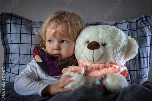 portrait sleepless girl todller lying bed with scarf around her neck on pillow with Teddy bear, child has a cold, is ill photo