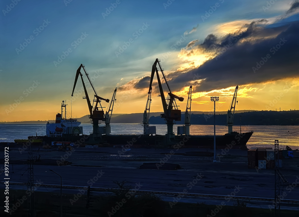 Silhouettes of cranes and ships at the port at sunset
