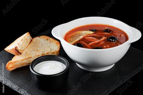 Solyanka. A plate of soup on a dark background with bread.