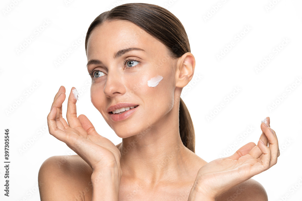 Close up of half naked woman applying anti age wrinkle serum, moisturizing lifting nourishing day cream on flawless skin, looking away, isolated on studio white background. Close up of half naked woman applying anti age wrinkle serum, moisturizing lifting nourishing day cream on flawless skin, looking away, isolated on studio white background.