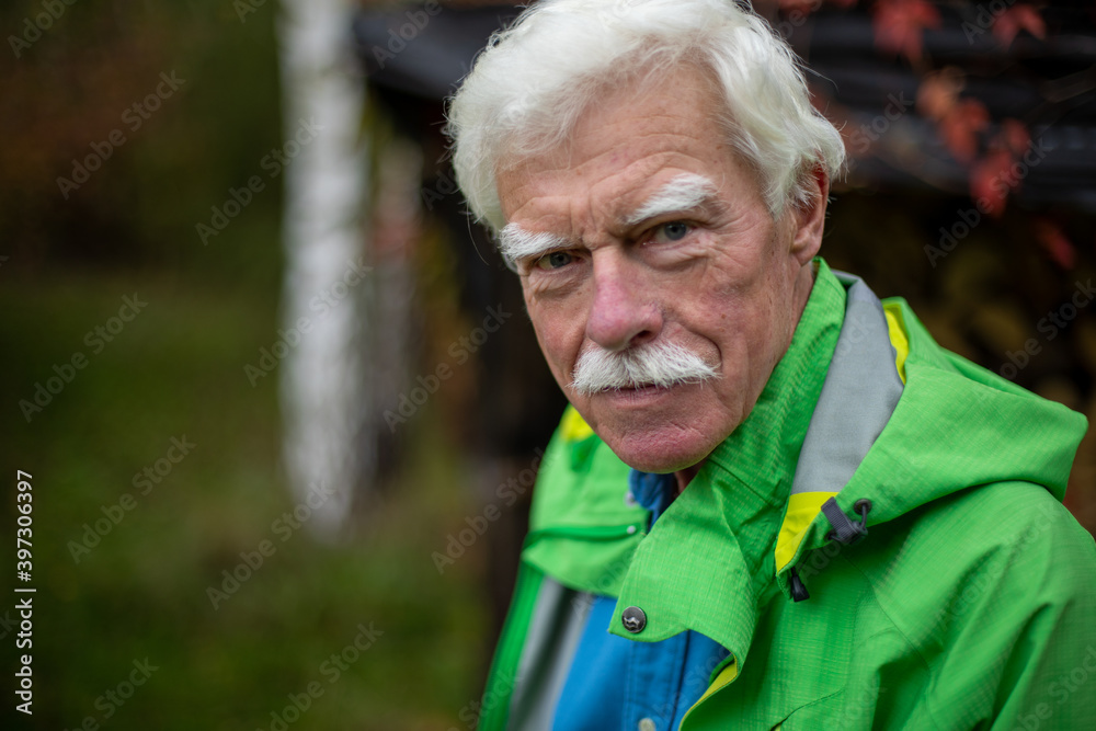 Outdoor portrait of a handsome senior man wearing a casual green jacket over the autumn background.