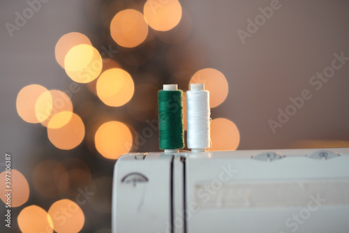 A close-up shot of two sewing threads, green and white, on the sewing machine and a Christmas tree on the background