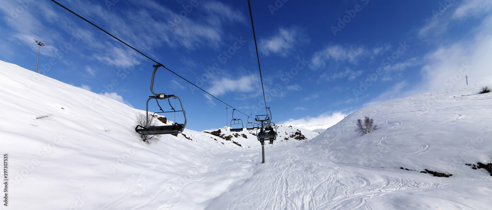 Panoramic view on chair-lift and snowy off-piste slope on ski resort at sun winter day