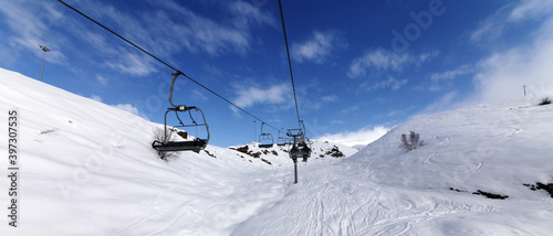 Panoramic view on chair-lift and snowy off-piste slope on ski resort at sun winter day