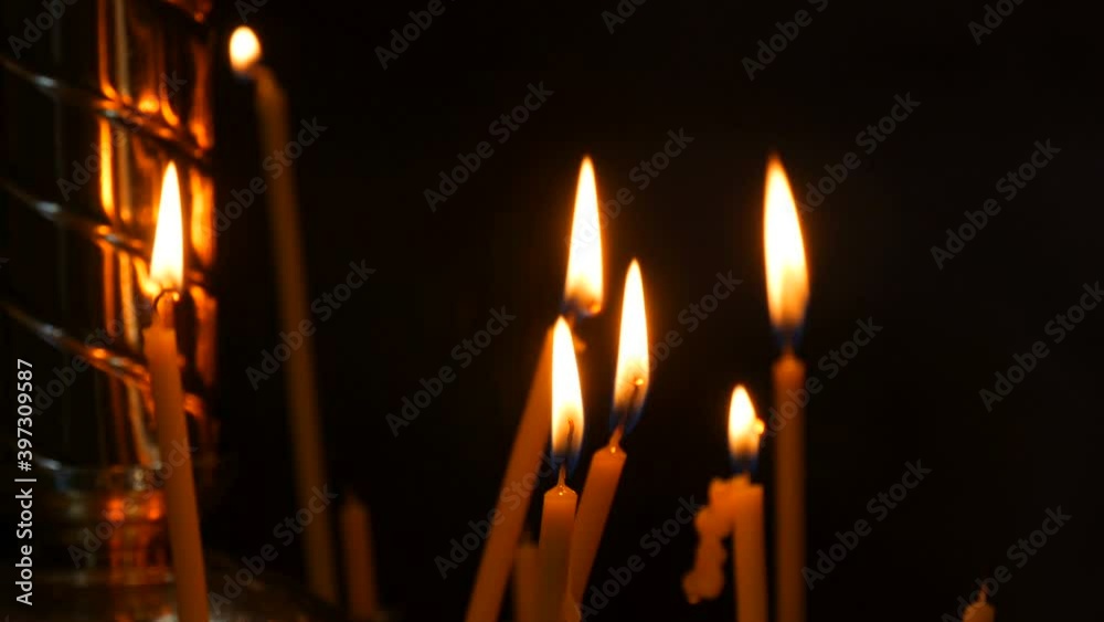 Long thin wax candles burn with a flame in an Orthodox church, memorial rituals for Christians. a woman's hand puts a candle in a special candlestick Long thin wax candles burn with a flame in an Orthodox church, memorial rituals for Christians. a woman's hand puts a candle in a special candlestick