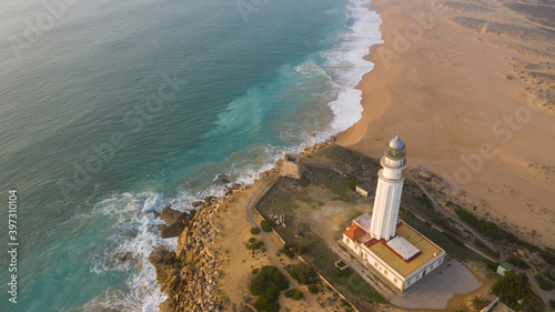 Drone views of the Trafalgar Lighthouse on the Costa de la Luz in Caños de Meca, Cadiz Andalucia, Spain. Faro de Trafalgar from above on a beautiful day with clouds and the blue sea.
