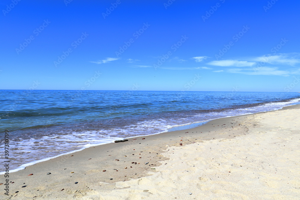 Calm blue Baltic sea and blue sky. A small long wide wave is approaching the sandy shore.. Donskoye, Svetlogorsk District