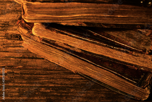 Obraz na płótnie Stack of old worn leather-bound books on textured wood background in candlelight. Selective focus. Low key. w salonie