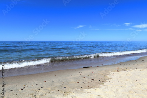 Calm blue Baltic sea. A small long wave with white foam is approaching the sandy shore. Blue sky. Donskoye  Svetlogorsk District