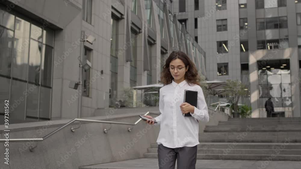 Business Woman. Young Girl In Business Style Clothes Goes Down The Stairs On The Street. She Has Phone And Notebook In Her Hands. Business Woman. Young Girl In Business Style Clothes Goes Down The Stairs On The Street. She Has Phone And Notebook In Her Hands.