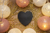 A black heart lies on yellow flowers surrounded by a Christmas garland with lights.
