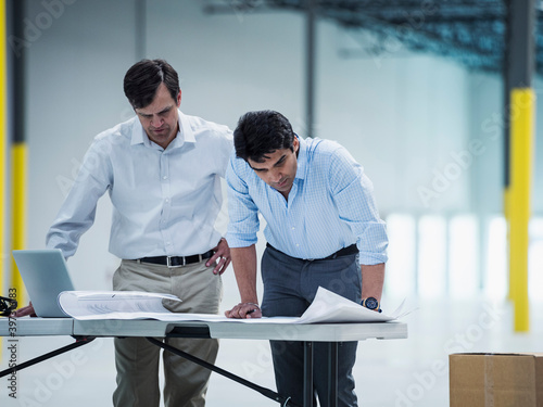 Architects using laptop and blueprint in warehouse photo