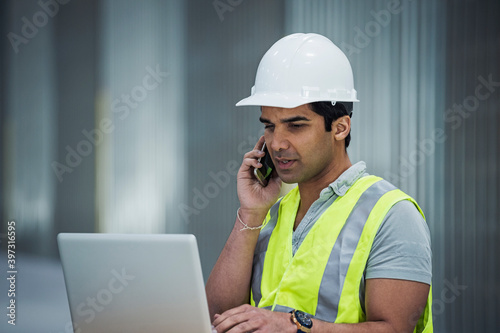 Indian worker using laptop and cell phone in warehouse