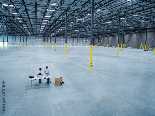 Architects using laptop and blueprint in empty warehouse