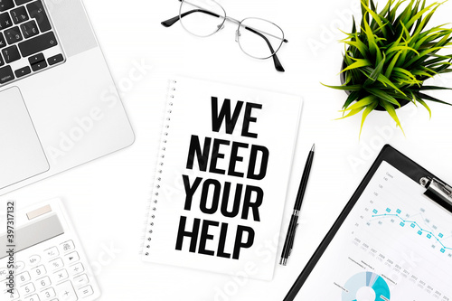 Text WE NEED YOUR HELP on card on office desk. Flat lay, top view.