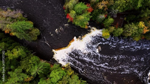 Aerial look down flying above the lower Tahquamenon Falls lowering down over the waterfall cascade in upper Michigan with colorful fall foliage and evergreen trees lining the river banks.