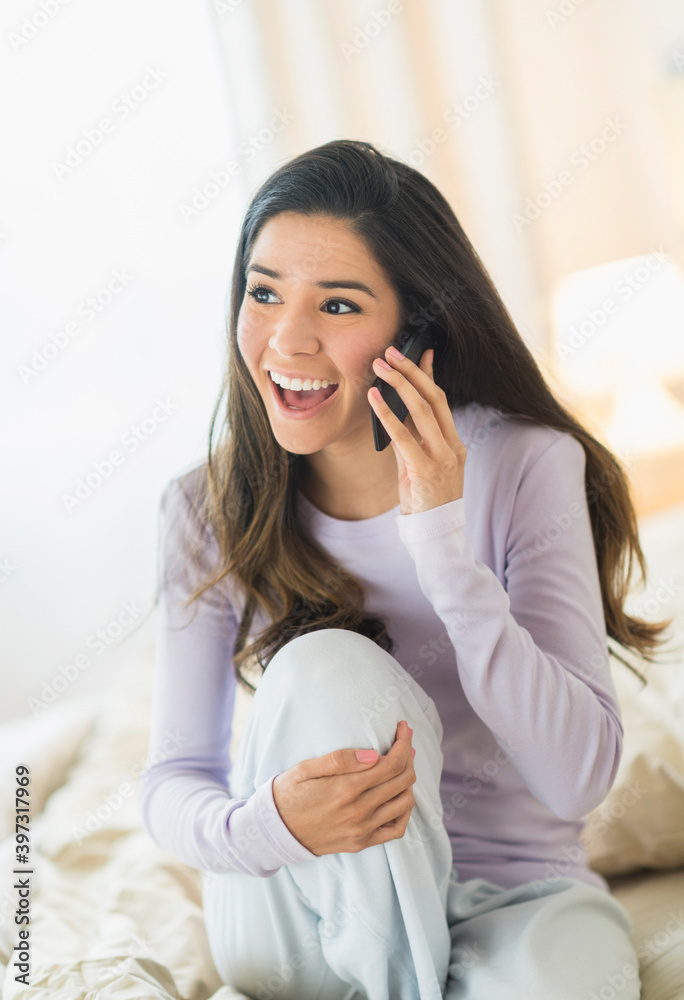 Enthusiastic Hispanic woman talking on cell phone in bed Enthusiastic Hispanic woman talking on cell phone in bed