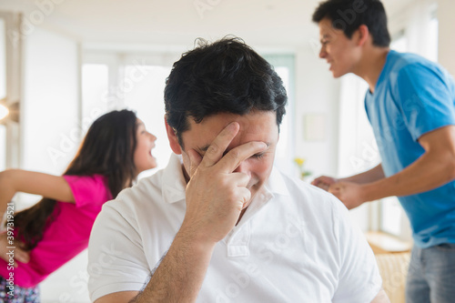 Hispanic father covering his face as children fight behind him photo