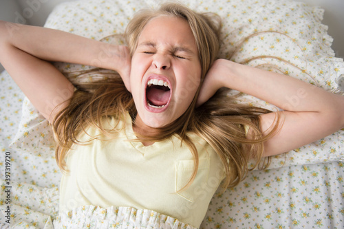 Shouting Caucasian girl covering her ears on bed photo