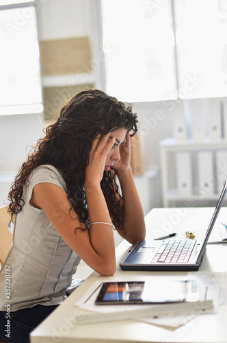 Frustrated mixed race businesswoman working on laptop at desk in office