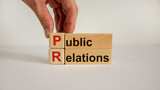 PR symbol. Wood cubes and blocks with words 'PR, public relations' on white background, copy space. Male hand. Business and public relations concept.