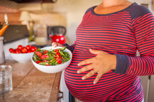 Pregnant Caucasian mother holding salad in kitchen photo