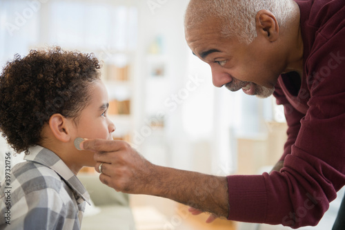 Mixed race grandfather pulling magic coin from ear of grandson photo