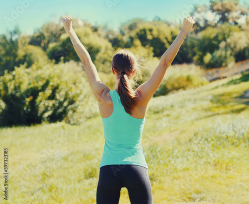 Fitness happy runner woman enjoying after training outdoors  runner winner  girl raising hands up  rear view