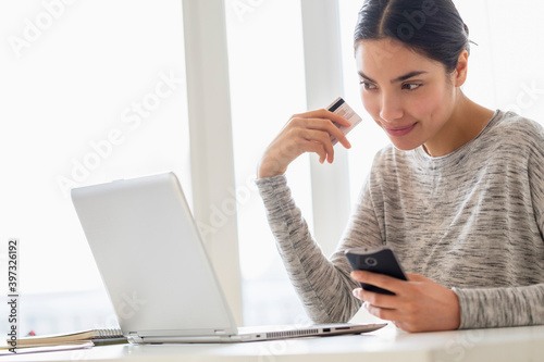 Hispanic woman shopping on cell phone and laptop
