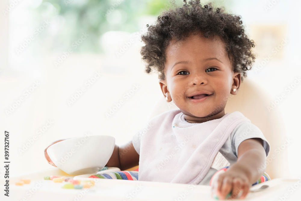 Smiling Black baby girl eating cereal from bowl in high chair Smiling Black baby girl eating cereal from bowl in high chair