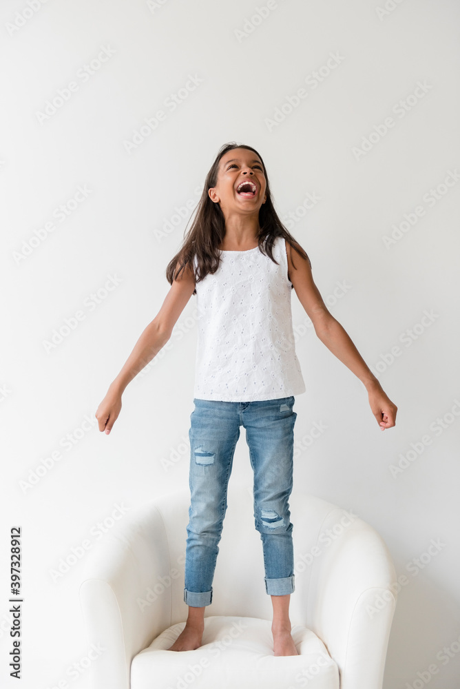 Mixed Race girl standing barefoot on armchair and shouting Mixed Race girl standing barefoot on armchair and shouting