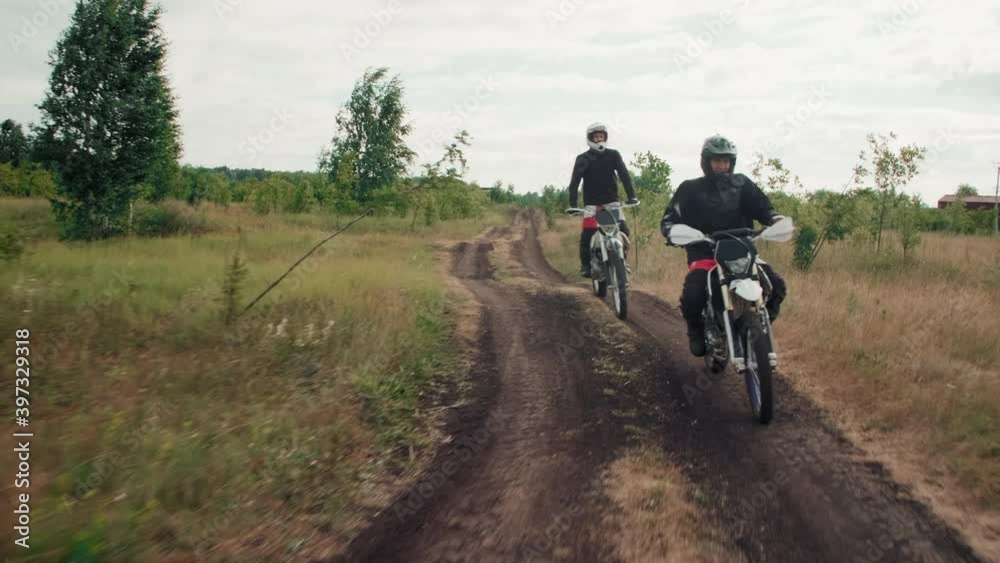Tracking shot of motorcyclists in gear and helmets riding together along dirt road Tracking shot of motorcyclists in gear and helmets riding together along dirt road