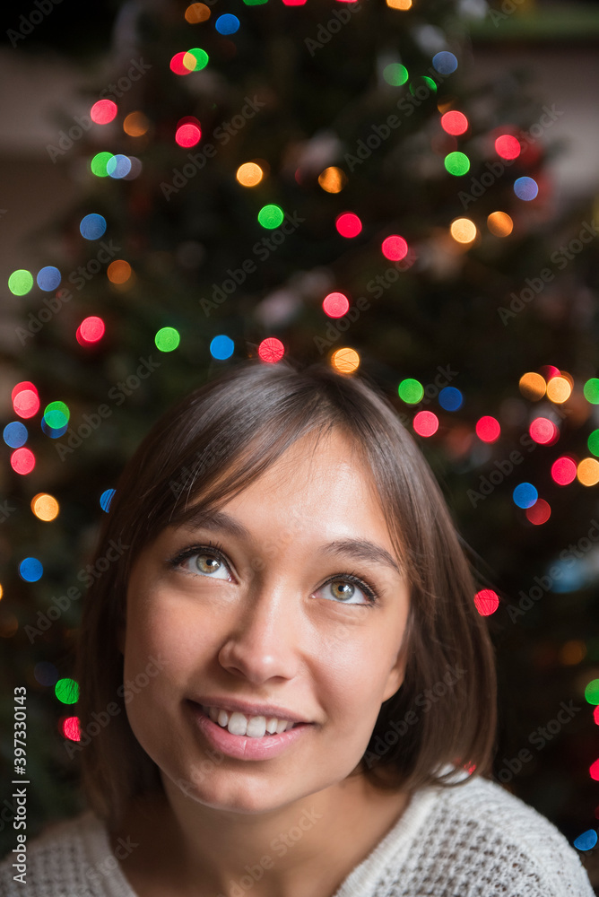 Pensive Mixed Race woman near Christmas tree