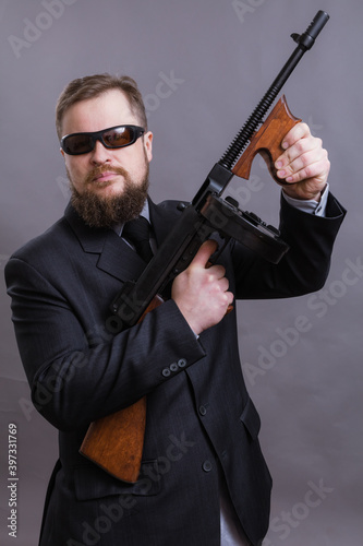 Mature man in sunglasses dressed in suit with tommy gun
