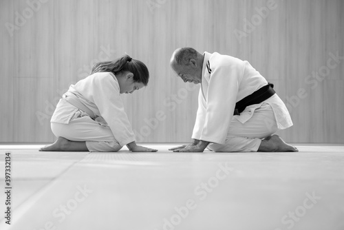 Old Judo master and young female student kneeling and bowing to each other