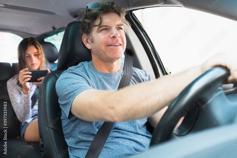 Man driving car, girl (10-11) texting in background
