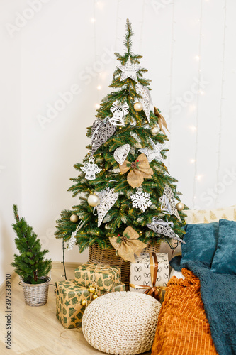 A cozy room decorated with garlands and Christmas trees. White pillow-bed is stylish and modern. Good New Year spirit. Light colors background texture place for text. Bedroom decor for the holiday