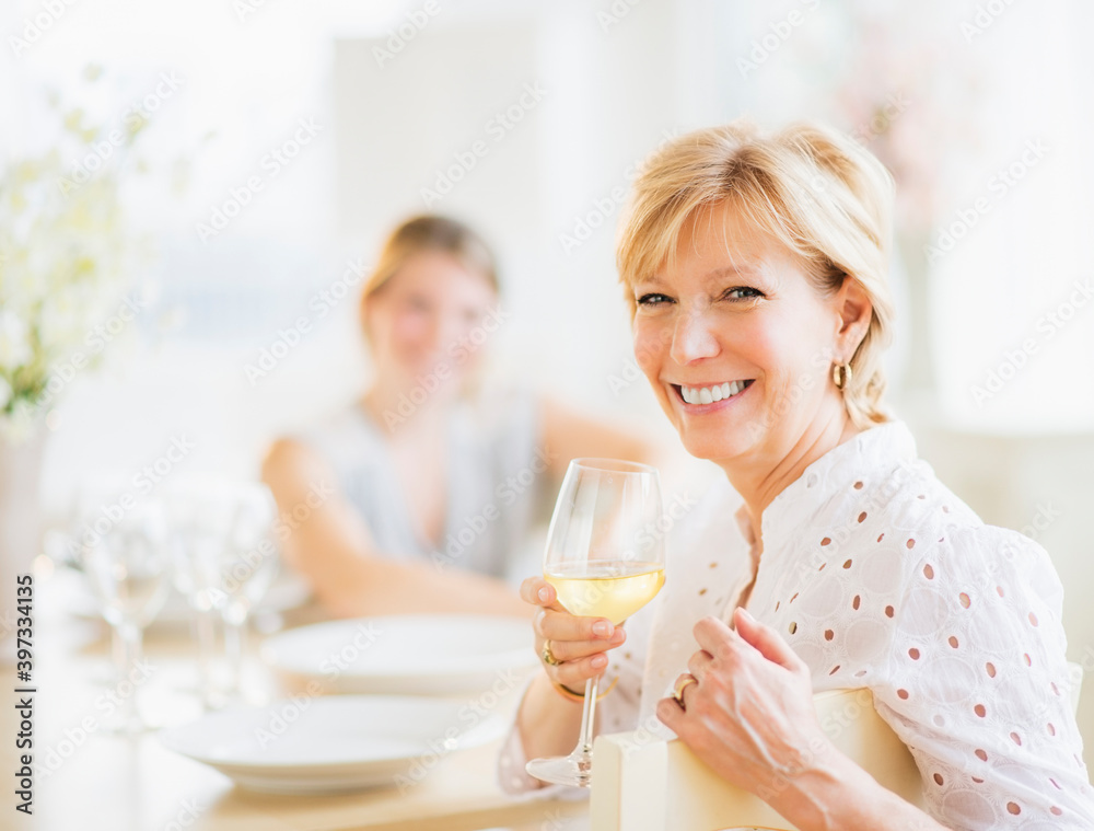 Mother drinking wine during dinner, out-of-focus daughter in background Mother drinking wine during dinner, out-of-focus daughter in background