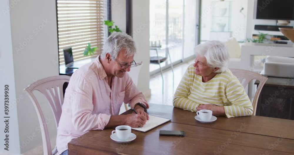Senior caucasian couple talking to each other calculating finances together at home Senior caucasian couple talking to each other calculating finances together at home