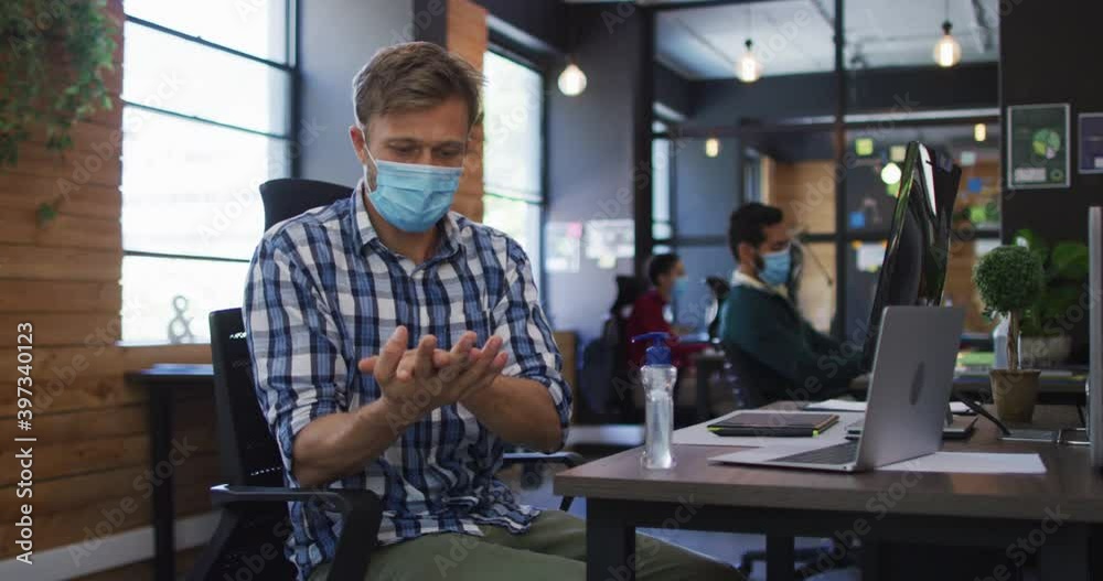 Caucasian man wearing face mask using hand sanitizing at modern office Caucasian man wearing face mask using hand sanitizing at modern office