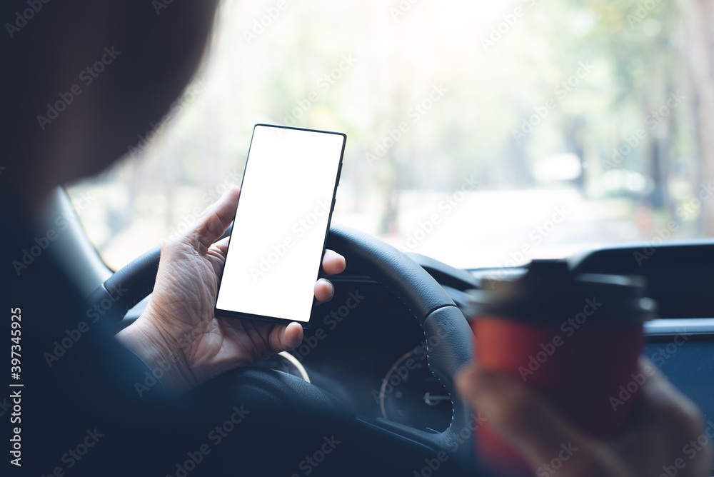 Mockup image of man hand holding and looking at blank screen mobile phone and drinking coffee inside a car Mockup image of man hand holding and looking at blank screen mobile phone and drinking coffee inside a car