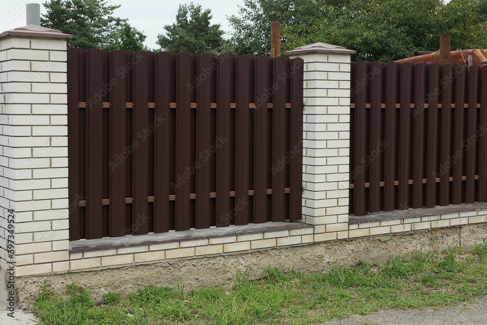 part of a wall of a fence made of brown metal and white bricks outside in green grass part of a wall of a fence made of brown metal and white bricks outside in green grass