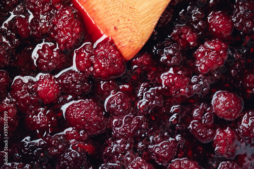 Close up of stirring blackberries and sugar making homemade blackberry jam with wooden utensil.