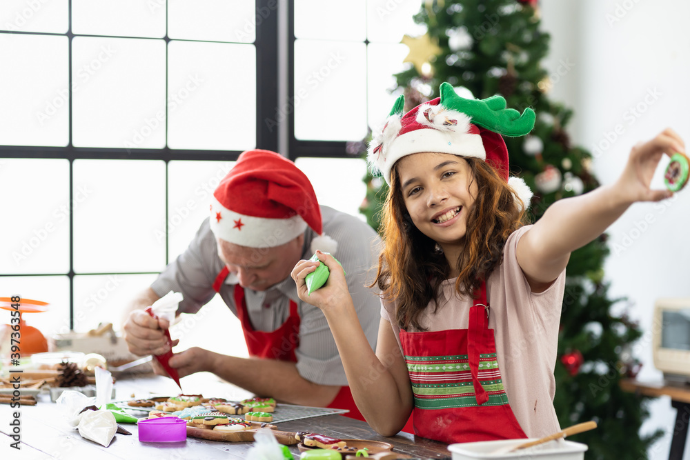 Happy family. Merry Christmas and Happy New Year. Father and daughter wearing Santa hat decorating Christmas gingerbread cookies together in kitchen at home. Cooking and Holiday concept Happy family. Merry Christmas and Happy New Year. Father and daughter wearing Santa hat decorating Christmas gingerbread cookies together in kitchen at home. Cooking and Holiday concept