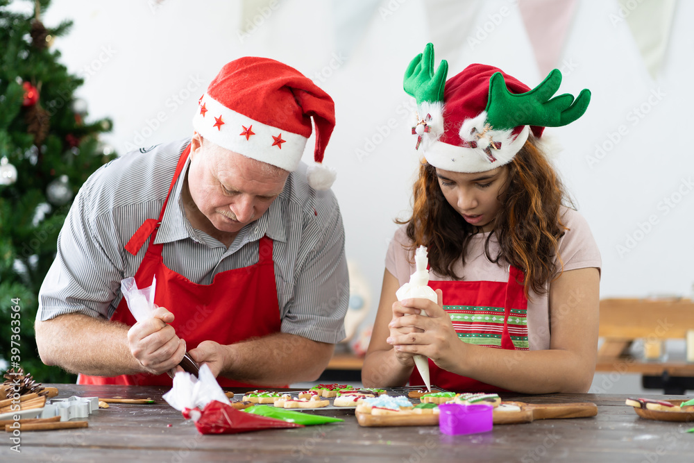 Happy family. Merry Christmas and Happy New Year. Father and daughter wearing Santa hat decorating Christmas gingerbread cookies together in kitchen at home. Cooking and Holiday concept
