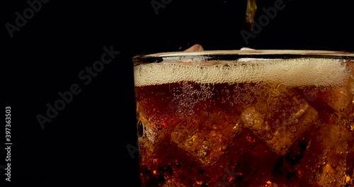 Truck shot of pouring carbonated drinks bubbles with ice cubes. Pouring soft drinks with ice and bubbles in glass on black background.