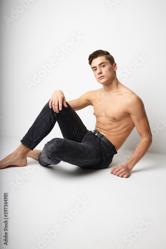 Handsome man sits on the floor bared muscular torso attractive isolated background