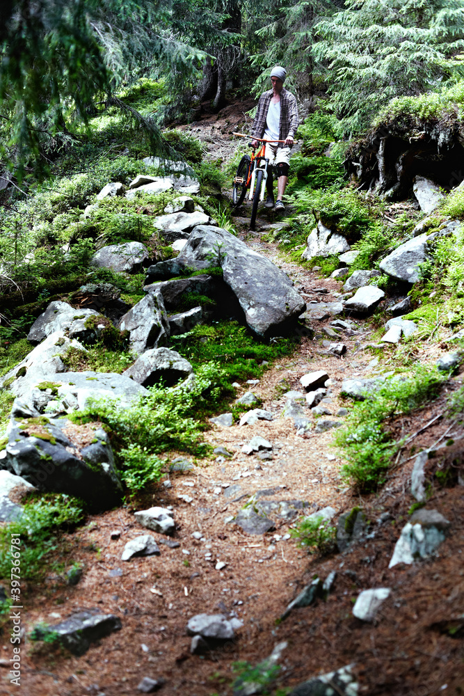 Fototapeta premium Young caucasian cyclist on a mountain bike rides along mountain trails in a mountain forest.
