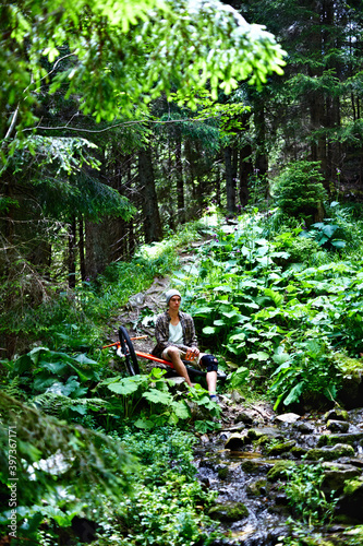 Young caucasian cyclist sitting near the bike in the summer mountain forest.