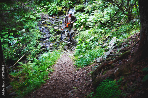 Mountain biker holding a bicycle in his hands crossing a mountain river 
